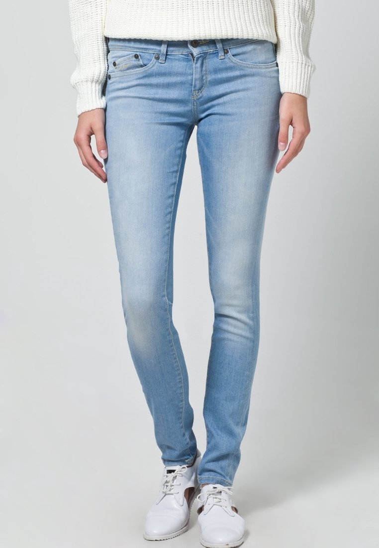 Light blue denim skinny jeans with a faded texture, five-pocket design, and a mid-rise waist, paired with white sneakers and a knit sweater.