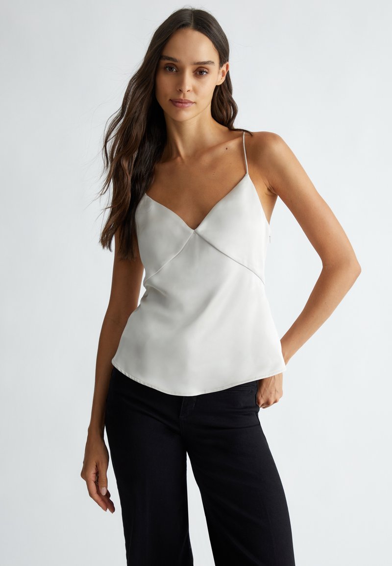 Top in satin grigio chiaro con spalline regolabili, scollatura a V e un design fluido e senza cuciture. Abbinato a pantaloni neri.