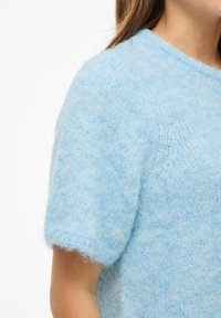 Lyseblå strikket genser med korte ermer, laget av mykt, lodent materiale. Har rund hals og delikat tekstur over hele genseren.