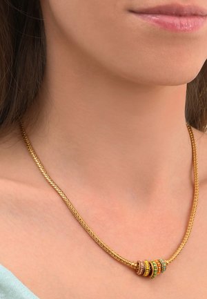 Collier en or tressé comprenant cinq anneaux texturés ornés de pierres multicolores, reposant sur un cou dénudé.