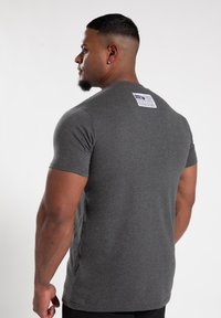 Graues T-Shirt mit kurzen Ärmeln und Rundhalsausschnitt, aus weichem Stoff gefertigt. Hat ein Etikett im oberen Rückenbereich mit Text. Einfaches und tailliertes Design.