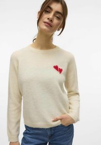 Maglione crema realizzato in morbido tessuto a maglia, con scollatura rotonda e maniche lunghe, caratterizzato da un design di cuore rosso sul petto.