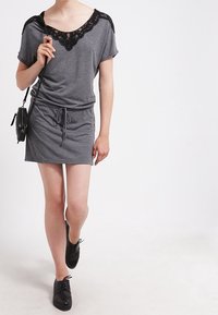 Szara sukienka wykonana z miękkiego materiału, z czarną koronkową wstawką przy dekolcie, krótkimi rękawami i ściągaczem w pasie. Połączona z czarnymi butami.