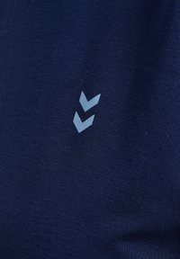 Donkerblauwe textuurstof met een opvallend lichtblauw chevronlogo dat aan de zijkant is gedrukt. Het ontwerp benadrukt een gladde, strakke uitstraling.