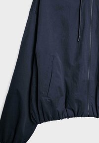 Veste zippée bleu marine foncé avec poche latérale et cordon de serrage à la taille, montrée sur un fond clair uni.