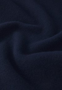 Marineblå fleece stof med en blød, tekstureret overflade, der viser bløde bølger og folder, som fremhæver dets bøjelige, varme egenskaber.