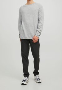 Pull gris à manches longues en coton avec un col rond, associé à un pantalon noir ajusté et des baskets grises et blanches.