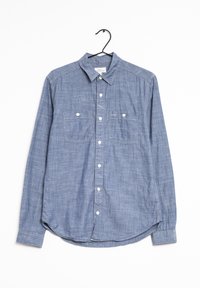 Vaaleansininen, pitkähihaisesta napitavasta valmistettu paita, joka on tehty chambray-kankaasta. Ominaisuuksiin kuuluvat kaksi rintataskua ja kaareva helma. Ripustettuna mustaan koukkuun.