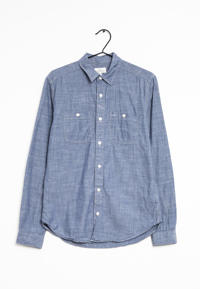 Vaaleansininen, pitkähihaisesta napitavasta valmistettu paita, joka on tehty chambray-kankaasta. Ominaisuuksiin kuuluvat kaksi rintataskua ja kaareva helma. Ripustettuna mustaan koukkuun.