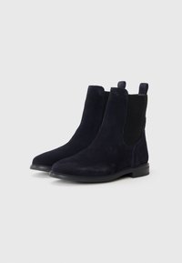 Botas de tobillo de ante azul marino con paneles laterales elásticos, puntera redondeada suave y un tacón bajo tipo bloque para mayor estabilidad. Diseño elegante pero funcional.
