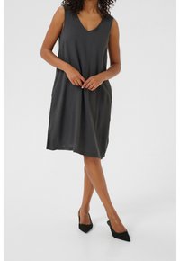 Ärmelloses, dunkelgraues Kleid mit V-Ausschnitt, knielang, aus weichem Stoff, mit Seitentaschen und lockerer Passform. Kombiniert mit schwarzen, spitzen Ballerinas.