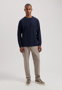 Marineblauses Hemd aus einem Baumwollgemisch mit langen Ärmeln, kombiniert mit hellbeigen Hosen. Die Schuhe sind grau mit hellen Akzenten. Einfaches, klares Design ohne Muster.