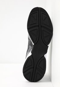 Scarpa atletica in bianco e nero con suola in gomma testurizzata, motivo a tasselli geometrico e parte superiore in rete. Presenta il marchio Nike.