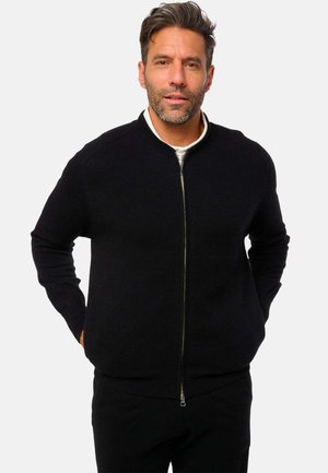 Schwarzer Reißverschluss-Pullover mit geripptem Kragen und Bündchen, der eine glatte Textur und ein minimales Design aufweist. Der Reißverschluss sorgt für einen funktionalen Akzent.
