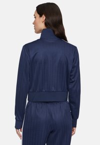 Marineblauwe sportjack met verticale streepjes, hoge kraag, ribgebreide manchetten en zoom. Soepele textuur, aangesloten pasvorm en strak ontwerp.