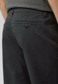 Donkergrijze broek met een gladde textuur, voorzien van een achterzak met een zwarte knoopdetail en riemlussen.