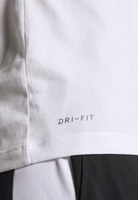 Närbild av ett vitt tyg med "DRI-FIT" tryckt nära fållen, bredvid kläder i svart och vitt med färgblock. 