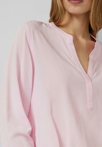 Jasnoróżowa bluzka z długim rękawem, z dekoltem w serek, wykonana z miękkiego materiału, z subtelnymi detalami przeszyć. Charakteryzuje się luźnym krojem i brakiem widocznych wzorów.