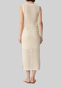 Beige knit two-piece set featuring a sleeveless top and a long skirt with side slits, made of openwork textured material.