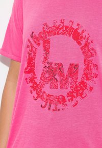 T-shirt a maniche corte, collo rotondo, di un vivace colore rosa brillante, con una grande grafica rossa decorata nel centro, caratterizzata da motivi floreali e paisley.