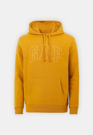 Musztardowa bluza z kapturem, przednią kieszenią i dużym obrysowanym logo "GAP" na klatce piersiowej.