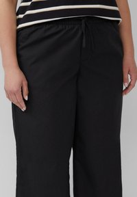 Schwarze, leichte Hose mit elastischem Bund und verstellbarem Kordelzug, im entspannten Schnitt und mit glatter Textur.