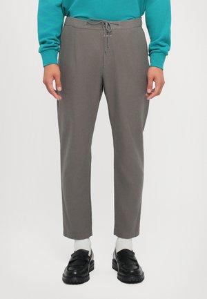 Pantaloni gri cu talie reglabilă, picioare tapered și buzunare laterale, asortați cu încălțăminte neagră și șosete albe. Textură de țesătură netedă.