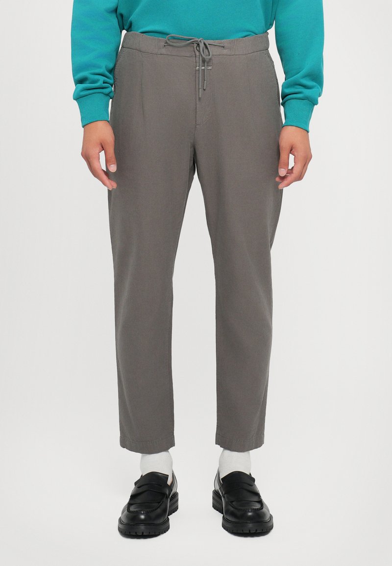 Gray trousers with a drawstring waist, tapered legs, and side pockets, paired with black shoes and white socks. Smooth fabric texture.