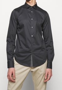 Svart skjorta med knappar och slim fit, med spetsig krage, långa ärmar och kontrasterande knappar. Slät tyg, böjd nederkant.