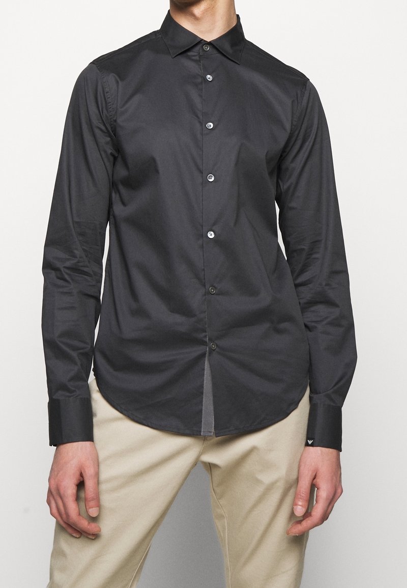 Svart skjorta med knappar och slim fit, med spetsig krage, långa ärmar och kontrasterande knappar. Slät tyg, böjd nederkant.