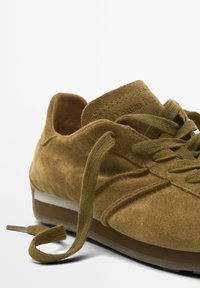 Baskets en daim marron avec bout arrondi, lacets plats et côtés texturés. Présente une semelle intermédiaire de couleur claire et une semelle extérieure en caoutchouc flexible.