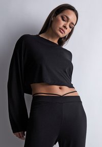 Haut noir court à manches longues avec un col rond, associé à un pantalon extensible taille haute avec des fines bretelles doubles à la taille.