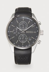 Montre chronographe en acier inoxydable argenté avec un cadran noir, un bracelet en cuir perforé noir et un affichage de date. Elle comprend trois sous-cadrans.