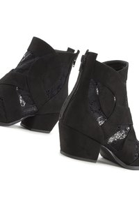 Melni potītes zābaki, izgatavoti no zamša ar mežģīņu paneļiem, ar ģeometrisku dizainu, vidēju papēdi un sānu rāvējslēdzēju vieglai uzvilkšanai.