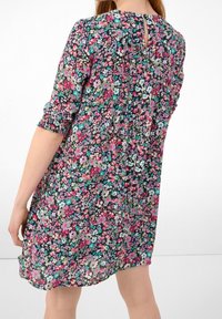 Blommig klänning med svart bakgrund och flerfärgade blommor, korta ärmar med elastiska manschetter och en nyckelhålsdetalj på baksidan.