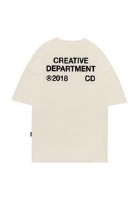 Krem majica oversized s velikim crnim natpisom na leđima: "KREATIVNI ODJEL 2018 CD." Kratki rukavi i opušteni kroj.