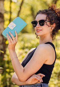 Turquoise wallet with a dotted closure, featuring a smooth texture and rectangular shape, held by a person against a blurred natural background.