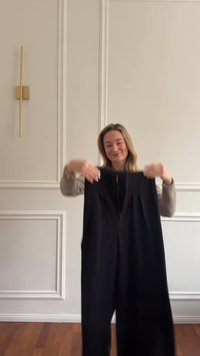 Combineu negru confecționat dintr-un material moale și fluid. Prezintă pliuri în talie și un fermoar frontal. Designul are picioare largi.