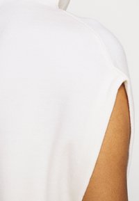 Weißes, ärmelloses Oberteil aus Baumwolle mit weicher Textur und lässiger Passform. Verfügt über einen runden Ausschnitt und seitliche Schlitze für Bewegungsfreiheit.