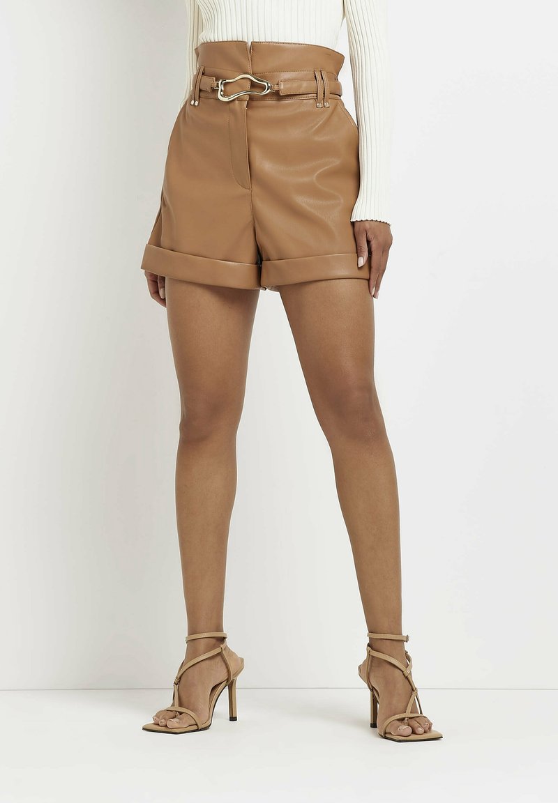 Femme portant un short en cuir marron clair à taille haute avec un ourlet retroussé, une ceinture assortie et des sandales à talons hauts beiges.
