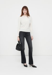 Lysfarget langermet polo-genser, mørke flared jeans, svart håndveske med samlet design, og spisse svarte hæler.