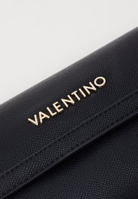 Portafoglio in pelle nera testurizzata con un prominente logo dorato "VALENTINO" sul davanti. Il design include dettagli di cucitura sottili.