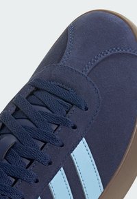 Marinblå mockaskor med ljusblå detaljer och snörning. Har rundad tå, broderade detaljer och en strukturerad gummisula.