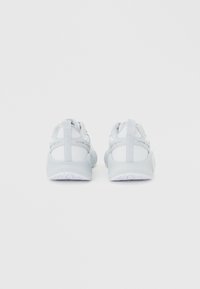 Ζευγάρι λευκά αθλητικά παπούτσια με χοντρά πέλματα, εμφανιζόμενα από πίσω σε απλό φόντο ανοιχτού γκρι χρώματος.