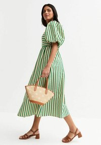 Vestido midi a rayas verde y crema con mangas abullonadas, combinado con un bolso de mimbre beige y sandalias de tacón cuadrado marrones.