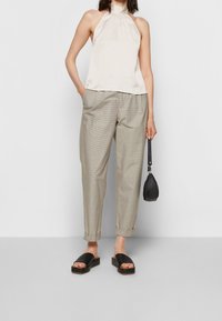 Haut halter beige clair, pantalons à carreaux beiges, et sandales à plateforme noires. Accentué par un petit sac à main noir. Design simple et épuré.