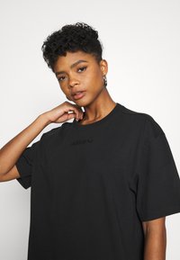 T-shirt in cotone nero con maniche corte e scollatura rotonda; presenta un logo in rilievo sul petto. Texture liscia, vestibilità comoda.