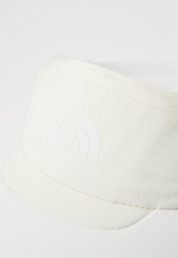 Valge müts, mis on valmistatud tekstureeritud materjalist, millel on ruuduline muster. Omab kumerat kulmu ja silmapaistvat valget logo "THE NORTH FACE".