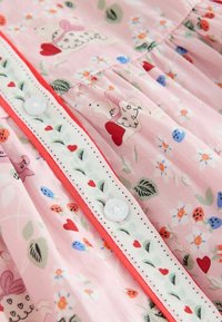 Roze stof met kleine knopen, versierd met witte schapen die rode harten vasthouden en een bloemmotief met rode, blauwe en oranje bloemen.