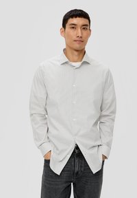 Weißes Hemd mit kleinen schwarzen Pünktchen, langen Ärmeln und spitzem Kragen, kombiniert mit dunklen Denim-Jeans.